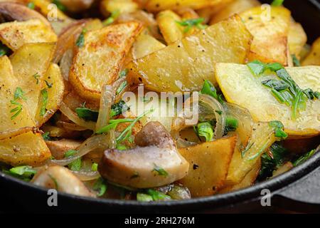 Pommes de terre frites maison avec des champignons et des oignons dans une poêle, sur fond noir Banque D'Images