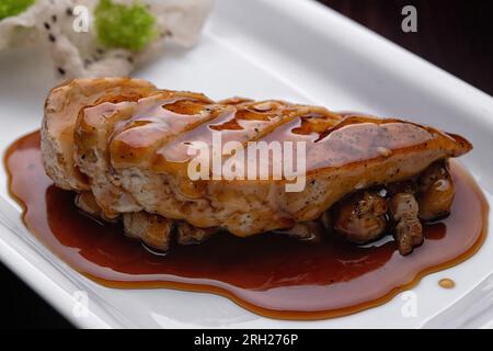 Filet de poulet à la sauce teriyaki, sur une assiette blanche, sur fond sombre Banque D'Images