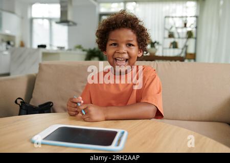 Portrait d'enfant heureux assis à table, dessin sur tablette Banque D'Images