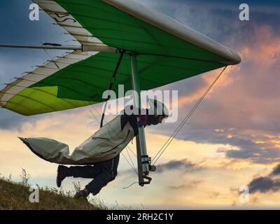 Le pilote du deltaplane court de la colline dans le ciel du coucher du soleil. Banque D'Images