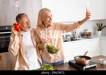 Couple mature avec des tomates prenant selfie dans la cuisine Banque D'Images