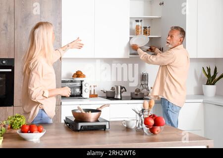 Femme mature et son mari prenant des assiettes dans la cuisine Banque D'Images