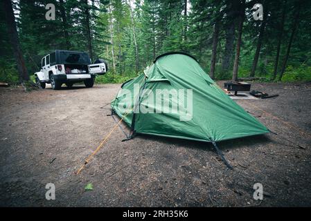 Une petite tente verte pour deux personnes est installée dans un espace de camping avec une voiture 4x4 à proximité dans une forêt de pins au Canada Banque D'Images