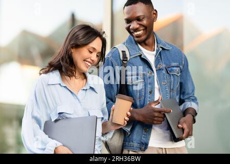 Heureux jeune couple multiracial marchant dans la rue, parlant et riant Banque D'Images