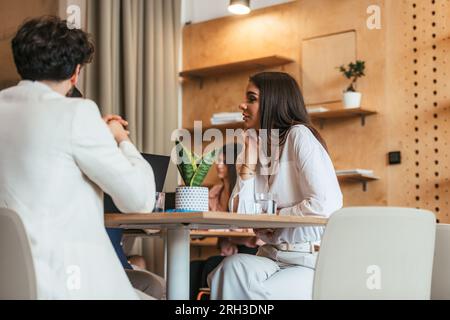 Jeune belle fille assise à la cafétéria du bureau et écoutant ses amis parler Banque D'Images