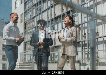 Jeunes gens d'affaires travaillant à distance par une journée ensoleillée, à l'extérieur, ayant une conversation amusante et riant Banque D'Images