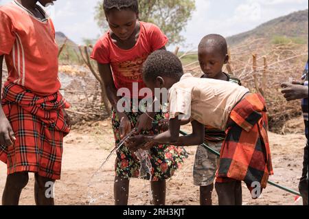 De jeunes enfants kenyans qui boivent à tour de rôle dans un tuyau d'eau douce avec de l'eau provenant d'un trou de forage voisin, dans le comté de Baringo, au Kenya Banque D'Images