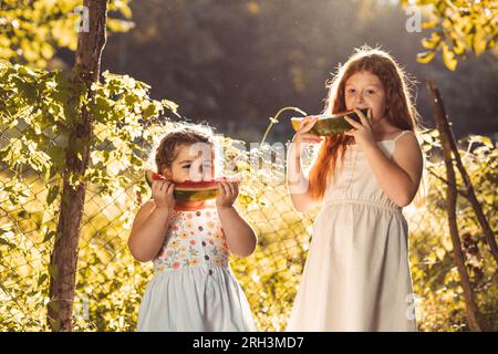 Deux petites filles, sœurs dehors en robes blanches, mangeant de la pastèque. Banque D'Images