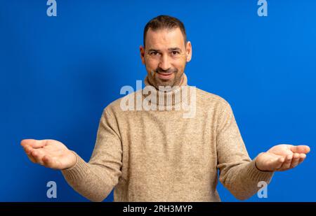 Homme hispanique barbu dans ses années 40 sur fond bleu regardant la caméra souriant avec les bras ouverts pour un câlin. Expression joyeuse embrassant le bonheur Banque D'Images