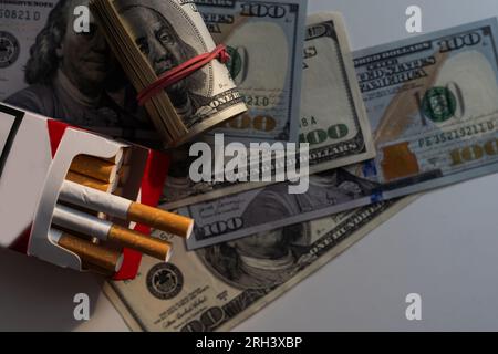 Paquet de cigarettes avec des billets de cent dollars sur un fond bleu. Frais de tabagisme Banque D'Images