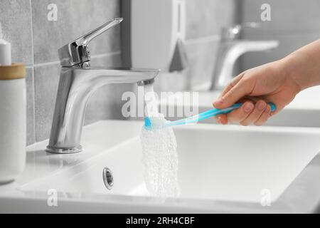 Femme lavant la brosse à dents en plastique sous l'eau qui coule du robinet dans la salle de bain, closeup Banque D'Images