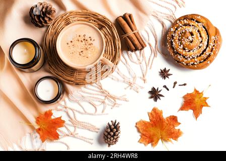 Concept esthétique d'automne. Tasse de café cappuccino avec cinnabon, bougies, plaid beige et feuilles d'automne sur fond blanc en gros plan. Banque D'Images