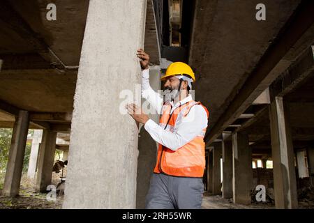 Portrait de jeune homme indien ingénieur civil ou architecte confiant portant casque et gilet inspectant et vérifiant la qualité du pilier en béton à con Banque D'Images