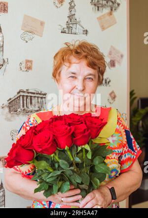 personne âgée adulte, femme blanche caucasienne âgée, grand-mère de 73 ans avec bouquet de roses rouges. Fête d'anniversaire, fête des mères. vue avant p Banque D'Images