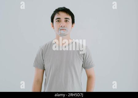 Photo de mise au point sélective d'un jeune homme asiatique portant un T-shirt décontracté vert sauge avec le visage couvert et l'expression plate avec de la crème à raser tout en regardant TH Banque D'Images
