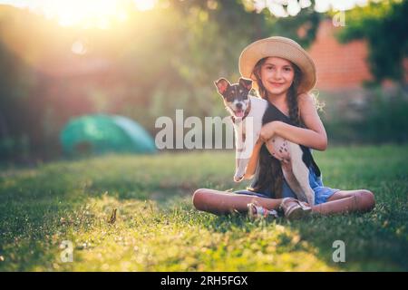 Fille heureuse jouant avec mignon chiot ludique petit chien en plein air sur une journée ensoleillée dans un parc Banque D'Images