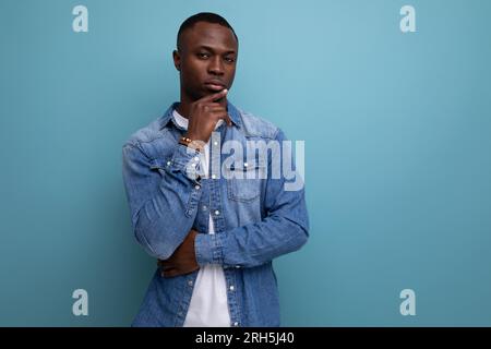 portrait d'un jeune beau homme américain de peau sombre habillé avec style dans des vêtements décontractés sur un fond bleu avec espace de copie Banque D'Images