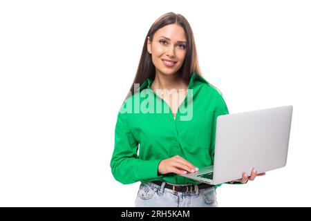 Adorable jeune femme careériste brun à poil brun avec maquillage dans un chemisier vert travaille à distance dans le domaine DE L'INFORMATIQUE Banque D'Images
