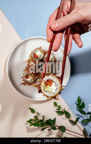 Une main d'homme tient des rouleaux de sushi japonais avec des baguettes Banque D'Images