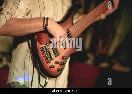 Plan rapproché d'une guitare basse jouée par un jeune homme d'une vingtaine d'années. L'accent est mis sur l'instrument, avec le visage du joueur non visible, emph Banque D'Images