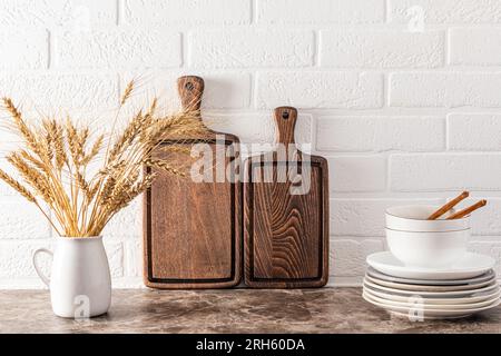 Deux belles planches à découper en bois sombre, une pile d'assiettes et une cruche blanche avec des épis de maïs sur un comptoir en marbre. espace cuisine éco-style Banque D'Images