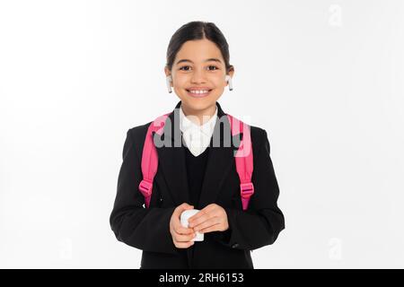 écolière souriante dans un étui de tenue uniforme et portant des écouteurs sans fil isolés sur blanc, joie Banque D'Images