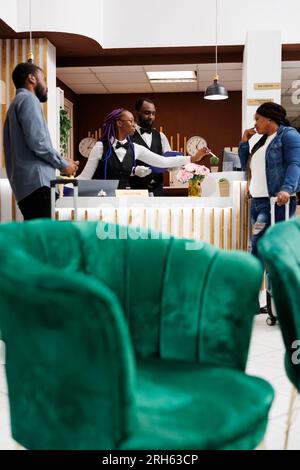 Jeune couple afro-américain arrivant à l'hôtel, debout à la réception avec des bagages parlant avec la réceptionniste pendant l'enregistrement. Agent de la réception obtenant des informations sur les clients à l'arrivée Banque D'Images