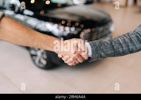 Gros plan recadré de l'achat réussi d'un véhicule, les acheteurs satisfaits méconnaissables serrent la main avec le vendeur masculin après avoir acheté une nouvelle voiture dans l'automobile Banque D'Images
