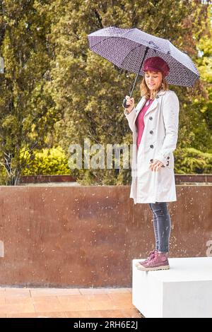 heureuse jolie femme avec parapluie regardant sa main sous la pluie Banque D'Images