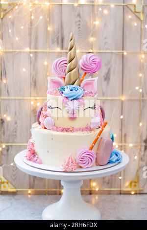 Gâteau licorne d'anniversaire à deux couches avec corne fondante dorée, cils et glaçage au fromage à la crème sur fond de bokeh de noël festif Banque D'Images