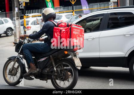 Salvador, Bahia, Brésil - 11 août 2023 : un livreur de nourriture APP est vu conduire une moto sur l'Avenida Bonoco parmi des voitures dans la ville de Salvado Banque D'Images