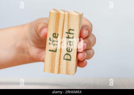 La vie et la mort. La main tient deux cubes en bois avec des inscriptions en gros plan. Isolez des rectangles avec des inscriptions sur blanc. Banque D'Images