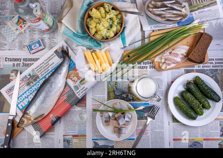 Russie, Moscou - 01 JUILLET 2023 : hareng, pommes de terre, bacon, pain, Stolichnaya vodka, bière et autres aliments sont servis sur un journal populaire au lieu d'un Banque D'Images