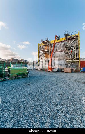 Un grand ascenseur de location orange avec son bras étendu au toit d'un bâtiment sur un chantier de construction. Il est utilisé pour transporter les matériaux de construction jusqu'au toit. Banque D'Images