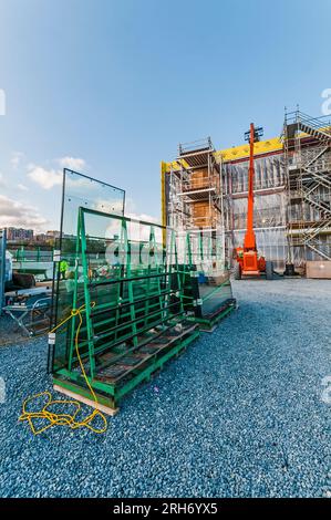 Un grand ascenseur de location orange avec son bras étendu au toit d'un bâtiment sur un chantier de construction. Il est utilisé pour transporter les matériaux de construction jusqu'au toit. Banque D'Images