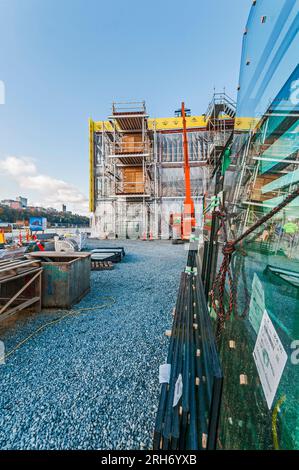 Un grand ascenseur de location orange avec son bras étendu au toit d'un bâtiment sur un chantier de construction. Il est utilisé pour transporter les matériaux de construction jusqu'au toit. Banque D'Images