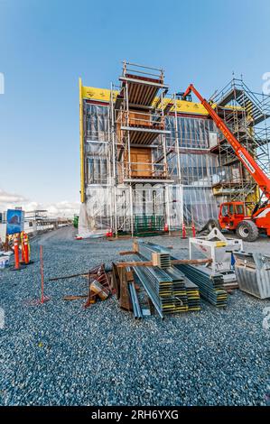 Un grand ascenseur de location orange avec son bras étendu au toit d'un bâtiment sur un chantier de construction. Il est utilisé pour transporter les matériaux de construction jusqu'au toit. Banque D'Images