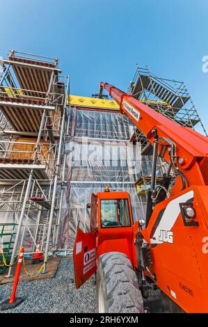 Un grand ascenseur de location orange avec son bras étendu au toit d'un bâtiment sur un chantier de construction. Il est utilisé pour transporter les matériaux de construction jusqu'au toit. Banque D'Images