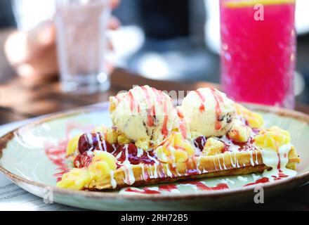 Gaufre belge avec glace à la vanille, sauce fraise, crème anglaise et caramel sur une assiette sur une table de restaurant. Gros plan de farine complète croustillante bel Banque D'Images