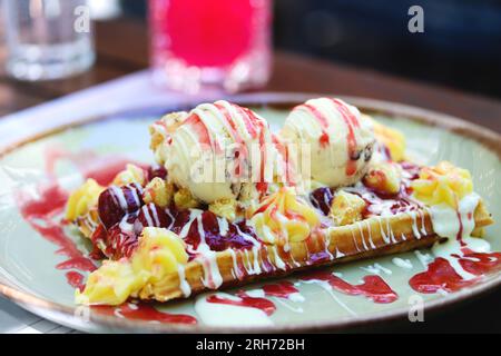 Farine complète gaufre belge croustillante avec une boule de crème glacée et garnitures. Gaufre belge avec glace à la vanille, sauce fraise, crème anglaise et ca Banque D'Images