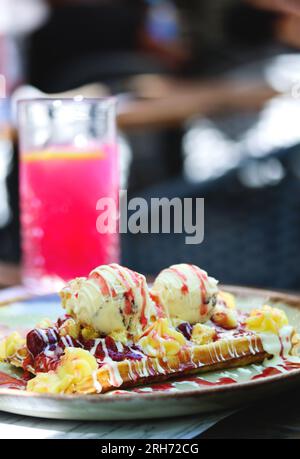 Gaufre belge avec glace à la vanille, sauce fraise, crème anglaise et caramel sur une assiette sur une table de restaurant. Gaufre belge croustillante à la farine complète Banque D'Images