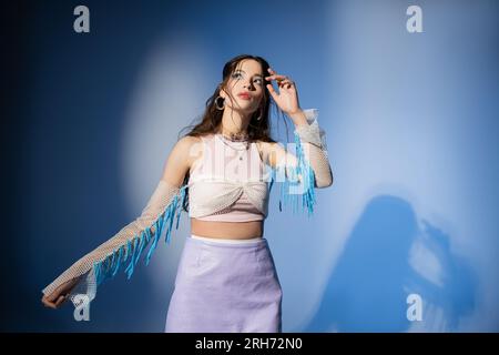 Jeune femme asiatique à la mode en jupe et dessus en maille posant sur fond bleu avec ombre Banque D'Images