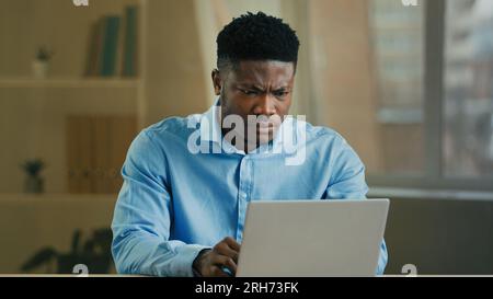 Contrarié homme afro-américain homme ethnique triste homme d'affaires travaillant ordinateur portable dans le bureau à domicile frustré travailleur en colère courtier entrepreneur perdu Internet sur Banque D'Images
