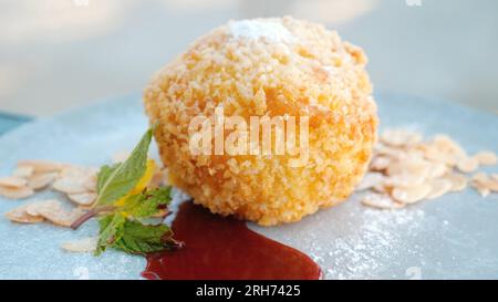 Crème glacée frite avec sauce fraise, noix d'amande et feuille de menthe sur assiette blanche. Banque D'Images