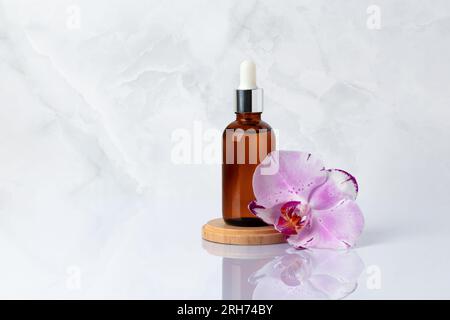 Bouteille en verre brun sur podium en bois et fleur d'orchidée rose gros plan. Huile de massage aromatique sur fond de marbre gris avec réflexion. Bio naturel s Banque D'Images