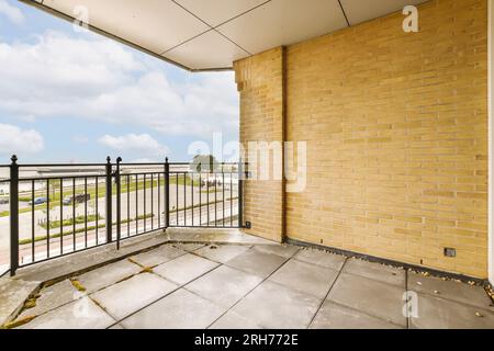 un balcon avec des murs de briques jaunes et des balustrades en métal noir sur le côté droit, donnant sur un parking vide Banque D'Images