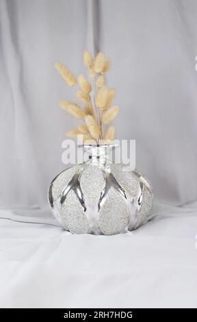 Herbe de queue de lapin sèche décorative dans un vase brillant sur tissu gris. Prise de vue verticale. Idée de concept de décoration. Banque D'Images