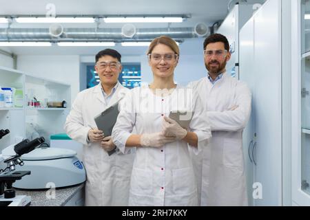 Portrait d'un homme et d'une femme debout dans le laboratoire, tenant des dossiers dans leurs mains, souriant et regardant avec confiance la caméra. Une équipe interethnique de scientifiques, chimistes et médecins. Banque D'Images