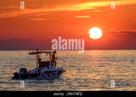 Les gens pêchent à partir d'un bateau alors que le soleil se couche sur la mer Adriatique au large de Trieste, en Italie. Crédit : Enrique Shore/Alamy stock photo Banque D'Images