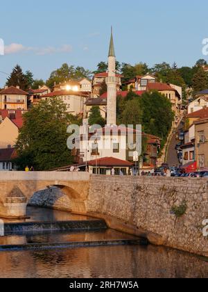 Pont sur la rivière Miljacka avec restaurant INAT Kuca et minaret derrière dans la ville de Sarajevo, Bosnie-Herzégovine, 14 août 2023. Banque D'Images